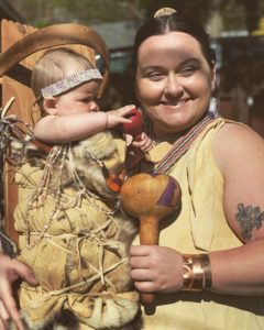 Diana Gates, a woman in traditional Native American clothing holds a baby in a cradleboard